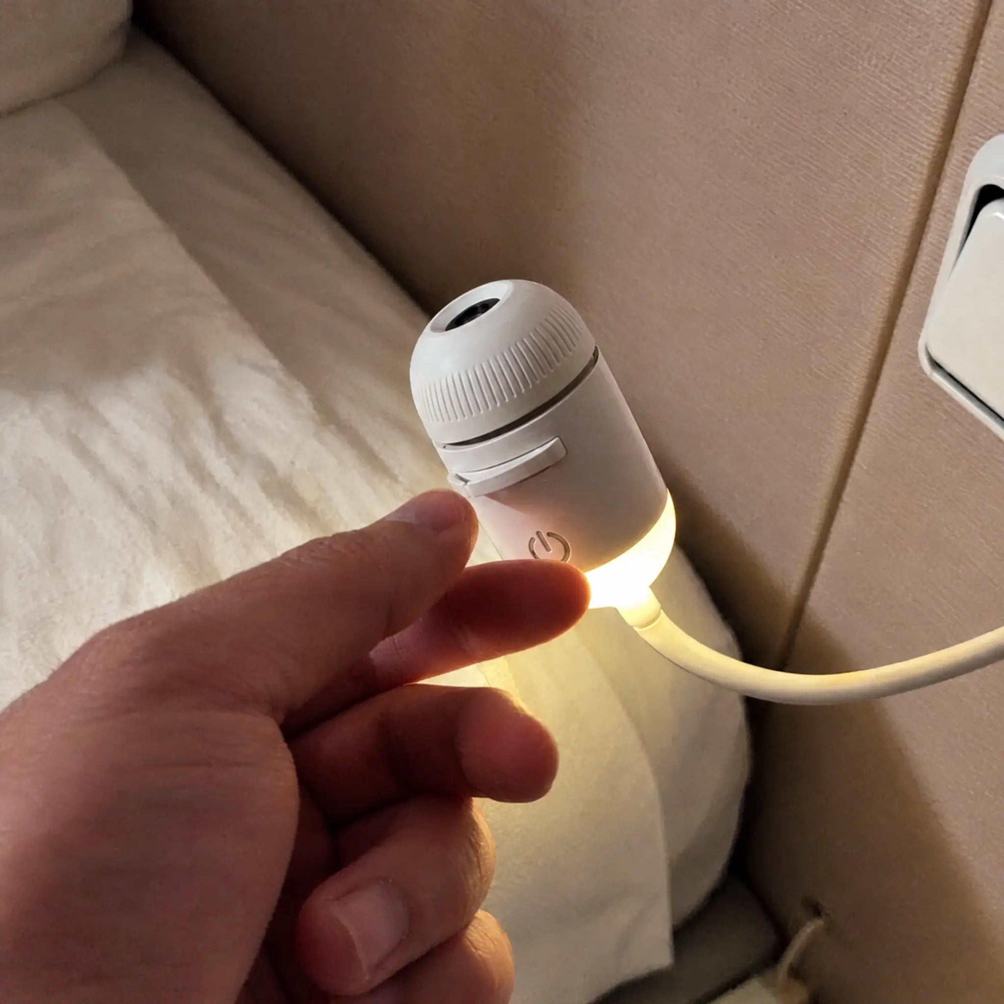 Hand pressing the power button beside a bed, warm glow